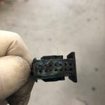 Gloved hand holding small corroded electrical connector