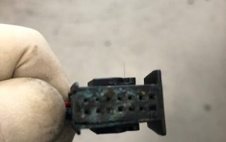Gloved hand holding small corroded electrical connector