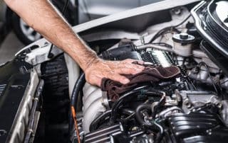 Hand wiping car engine under open hood
