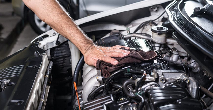 Hand wiping car engine under open hood
