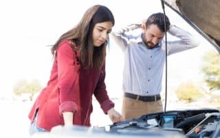 Couple looking under car hood with concern