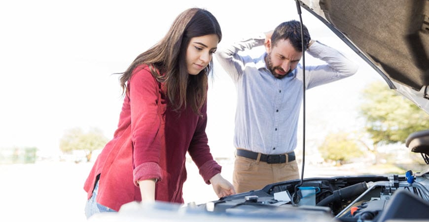 Couple looking under car hood with concern