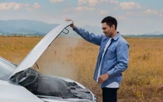Man inspecting smoking car engine in field