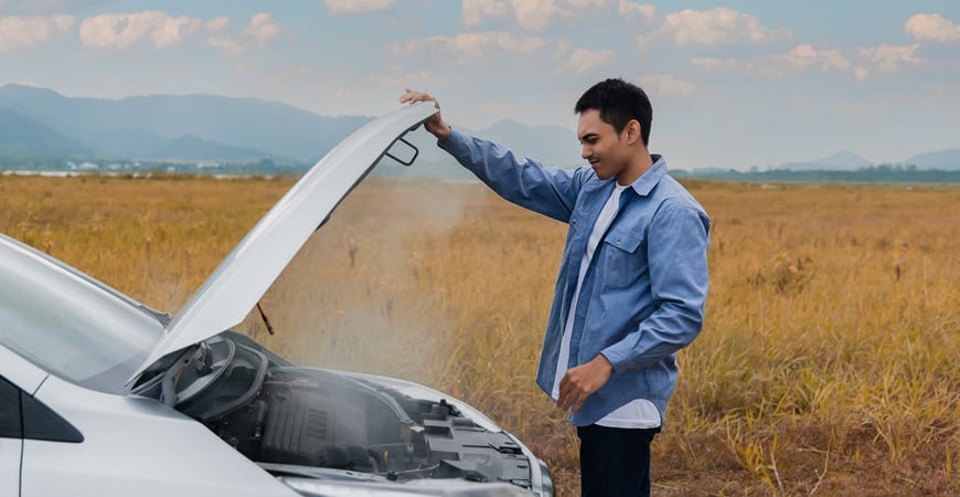 Man inspecting smoking car engine in field