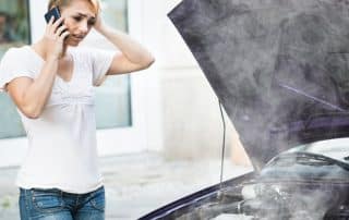 Woman on phone beside smoking car engine