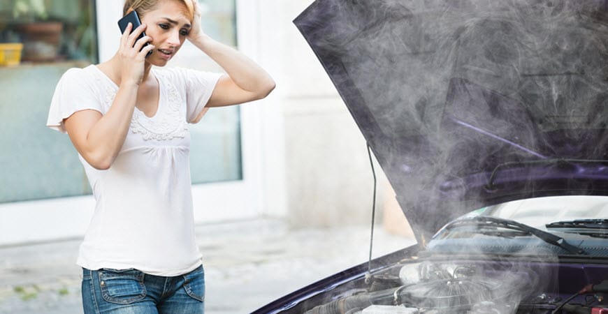 Woman on phone beside smoking car engine