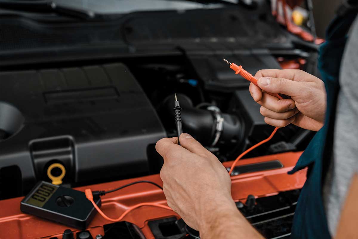Mechanic testing car battery with multimeter probes