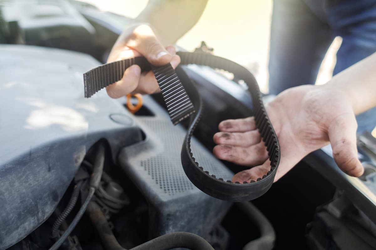 European Auto Cambelt Timing Belt Replacement in Denver image Mechanic holding worn timing belt over car engine