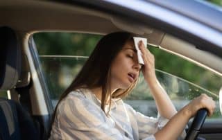 Woman wiping forehead while sitting in car