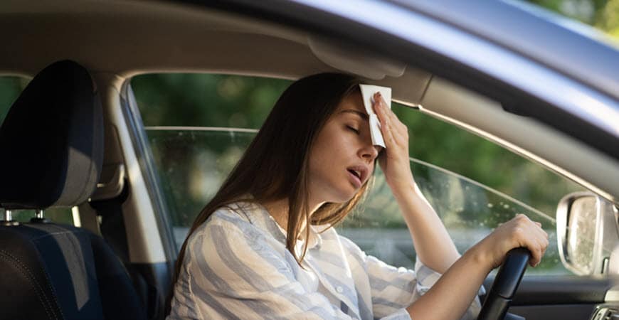 Woman wiping forehead while sitting in car