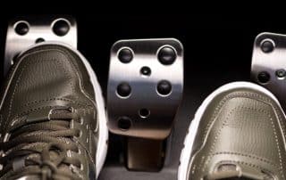 Sneakers pressing car pedals in vehicle footwell