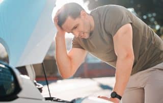 Man stressed over broken car with hood open