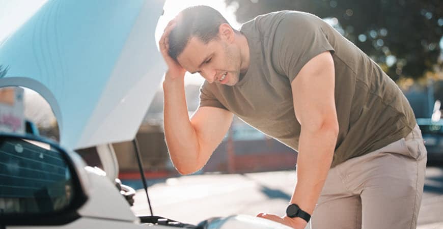 Man stressed over broken car with hood open