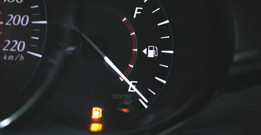 Car dashboard fuel gauge near empty with warning light
