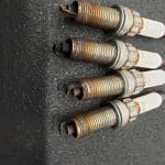 Four used spark plugs on dark surface