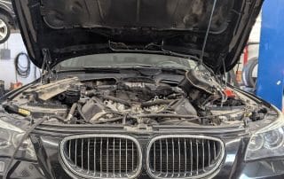 Black BMW with hood open in auto shop