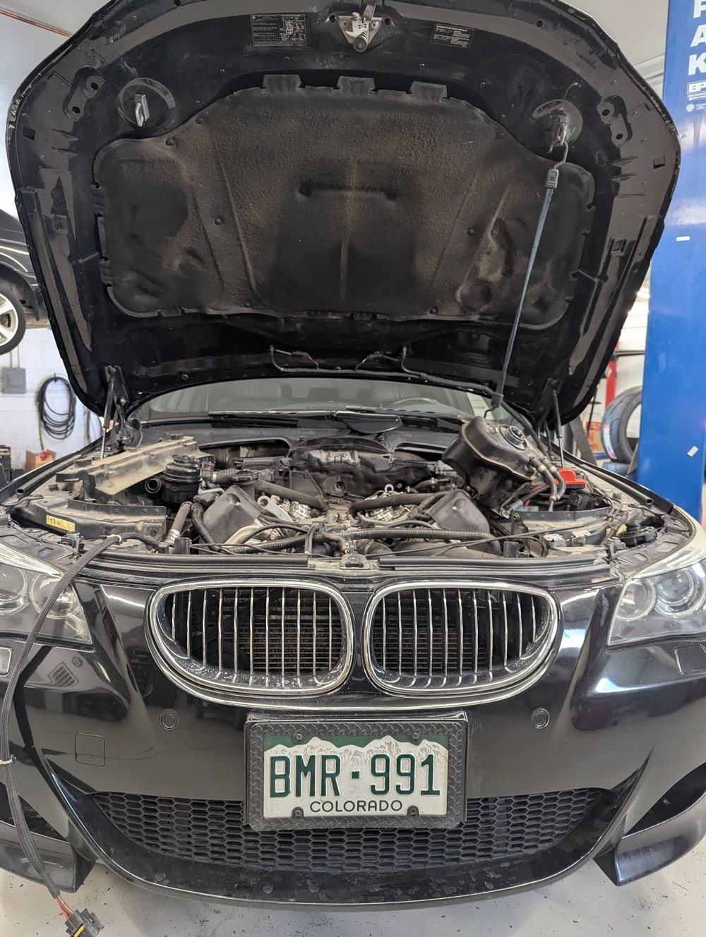 Black BMW with hood open in auto shop
