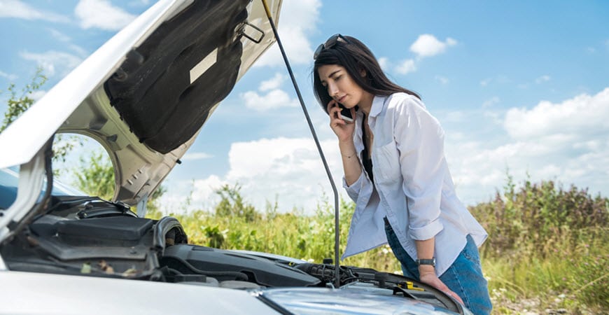 Woman on phone beside broken-down car