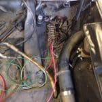 Car engine bay with exposed wiring and fuse panel