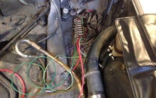Car engine bay with exposed wiring and fuse panel