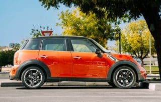 Orange compact car parked under tree on street