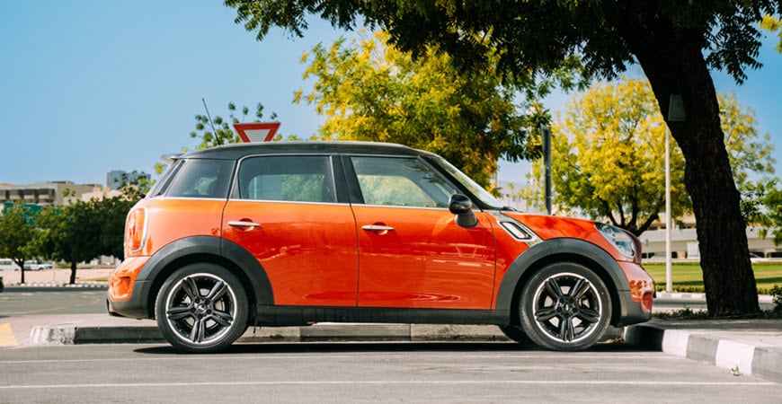 Orange compact car parked under tree on street