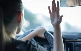 Woman driving car waving hand inside vehicle