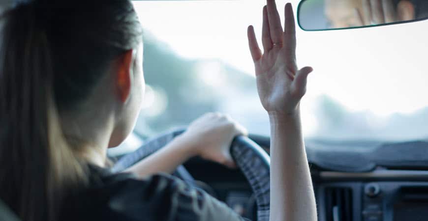 Woman driving car waving hand inside vehicle