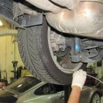 Mechanic inspecting car suspension and tire underneath vehicle