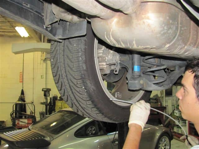 Mechanic inspecting car suspension and tire underneath vehicle