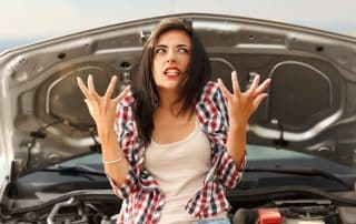Frustrated woman standing by car with open hood