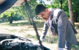 Man in suit inspecting car engine outdoors