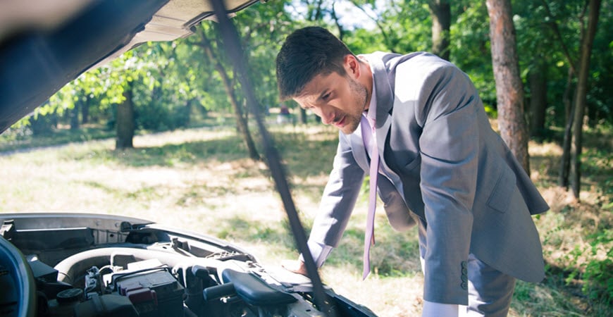 Man in suit inspecting car engine outdoors