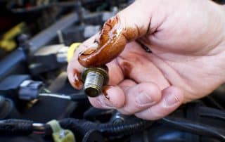 Hand holding oil-covered bolt over car engine