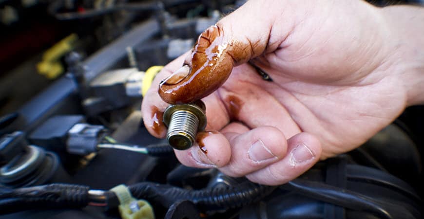 Hand holding oil-covered bolt over car engine