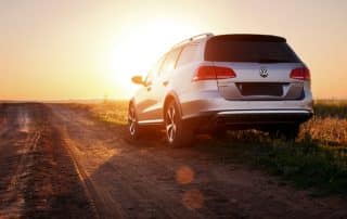 White Volkswagen SUV on rural dirt road at sunset