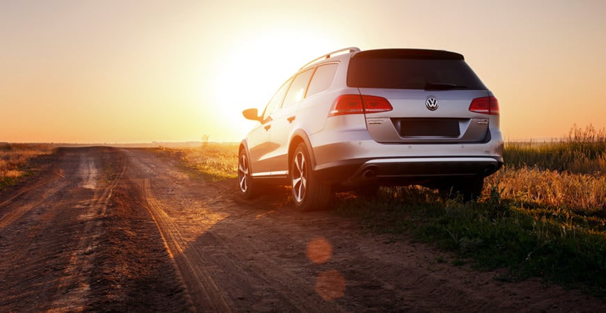 White Volkswagen SUV on rural dirt road at sunset