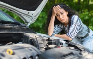 Worried woman looking at car engine under open hood