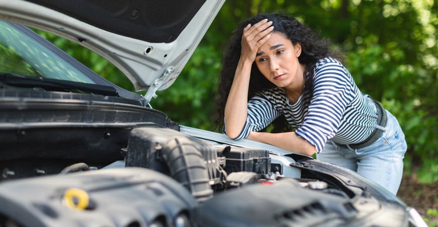 Worried woman looking at car engine under open hood