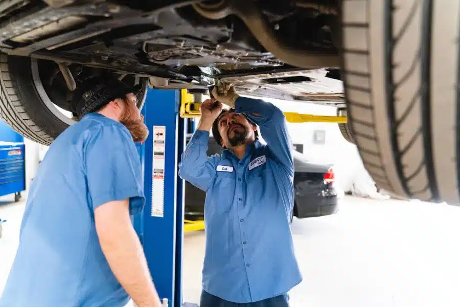 Two mechanics inspecting car underside in auto shop