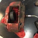 Red brake caliper on workbench with tool