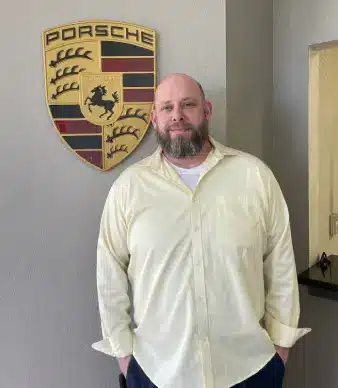 Man standing beside Porsche logo wall emblem