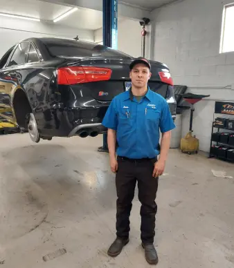 Mechanic standing in auto shop with lifted car